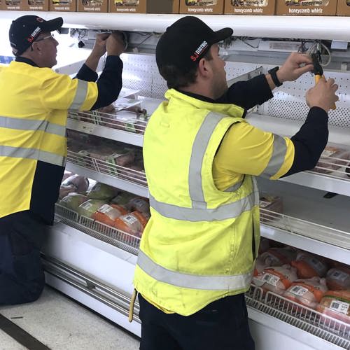 two men working on refrigerator at supermarket